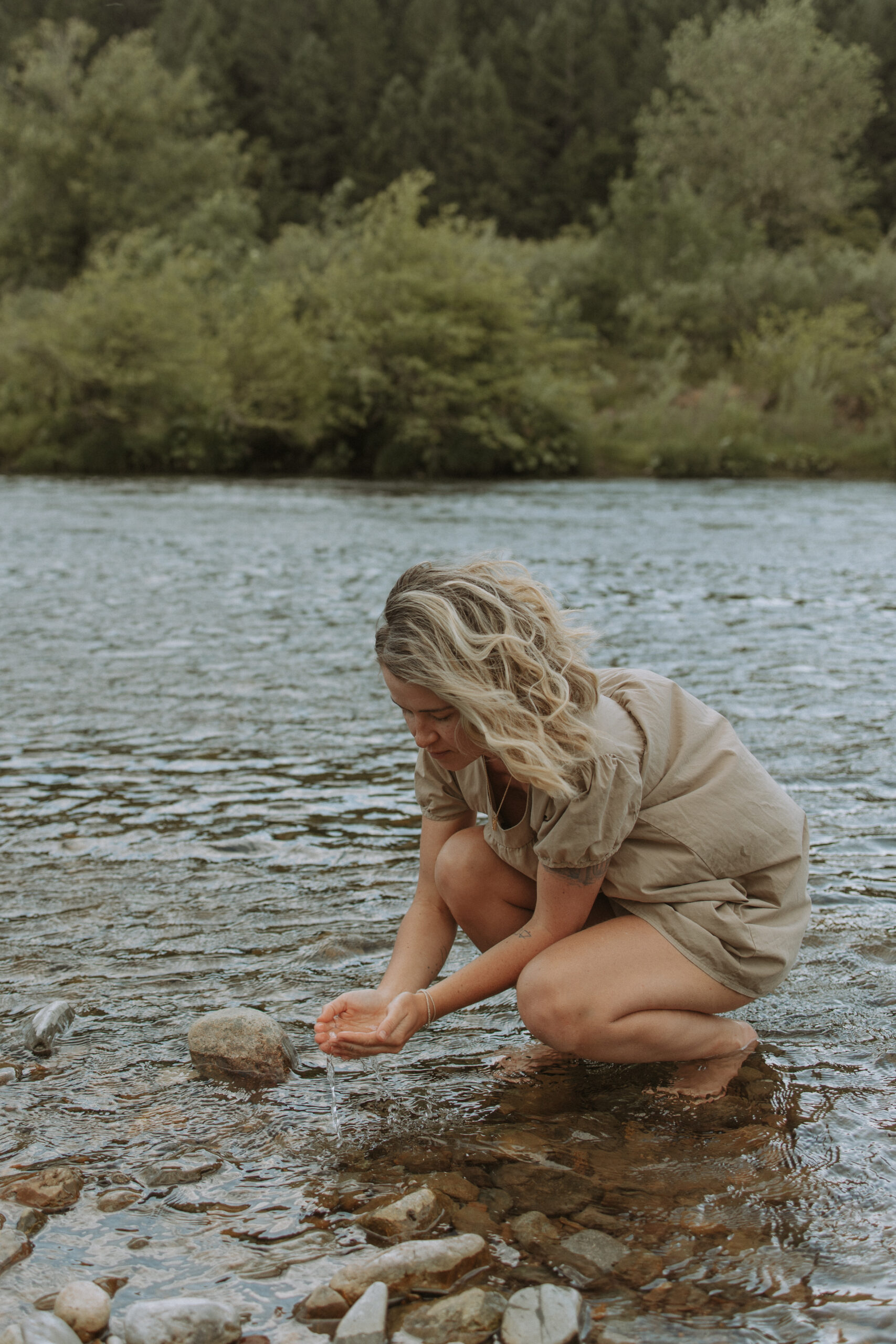 Blonde woman crouching down in river, holding water between her cupped palms